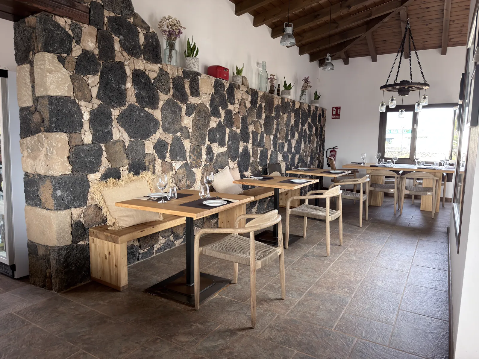 Comedor interior con pared de piedra volcánica y mesas de madera